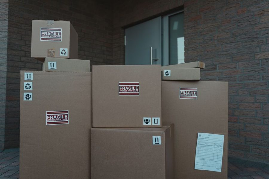 Caixas de papelão empilhadas na entrada de um prédio, uma delas com a via do pedido colada